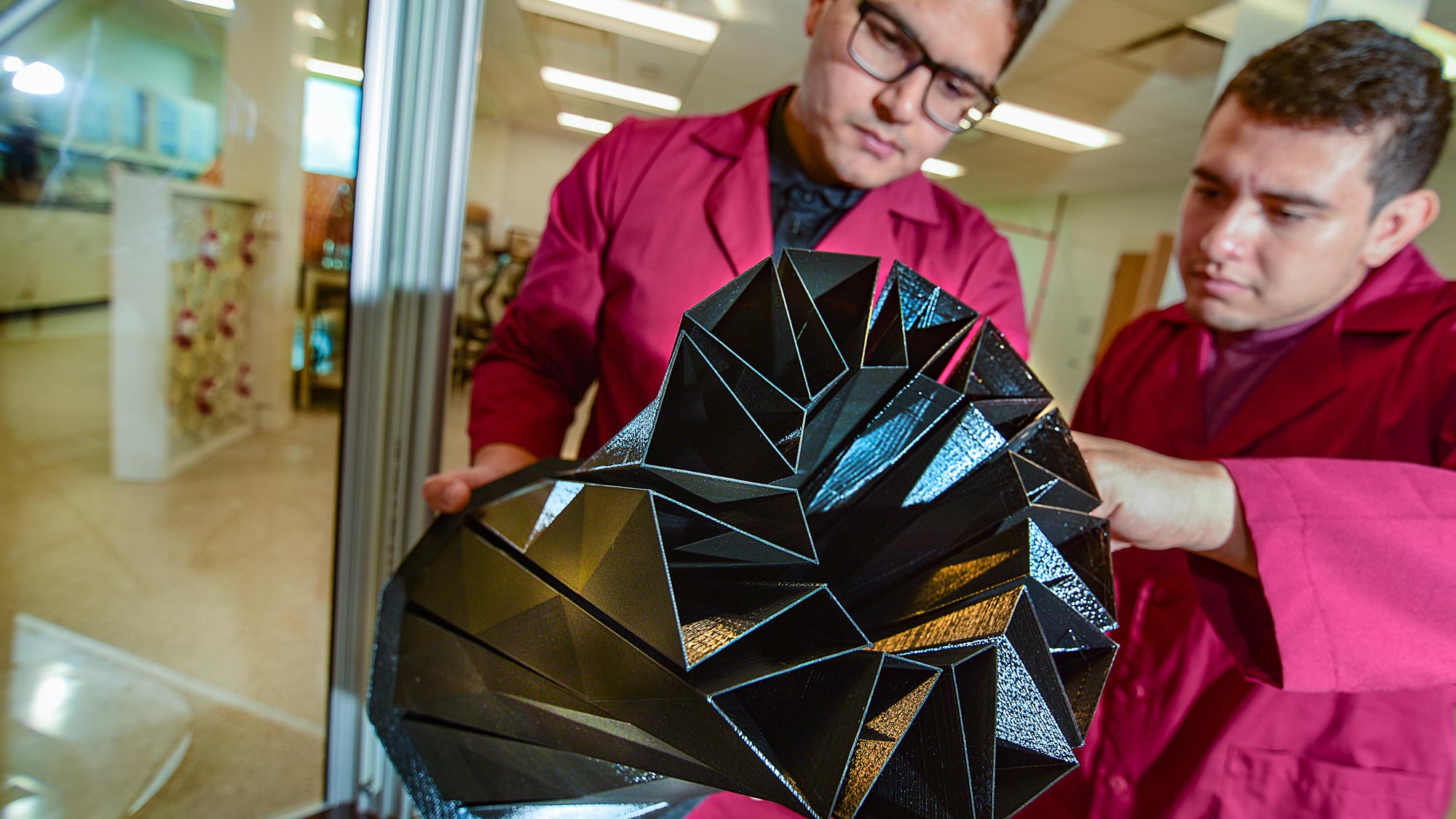 Two male researchers at the Center for Infrastructure Renewal examine a black device with several geometric shapes within it.