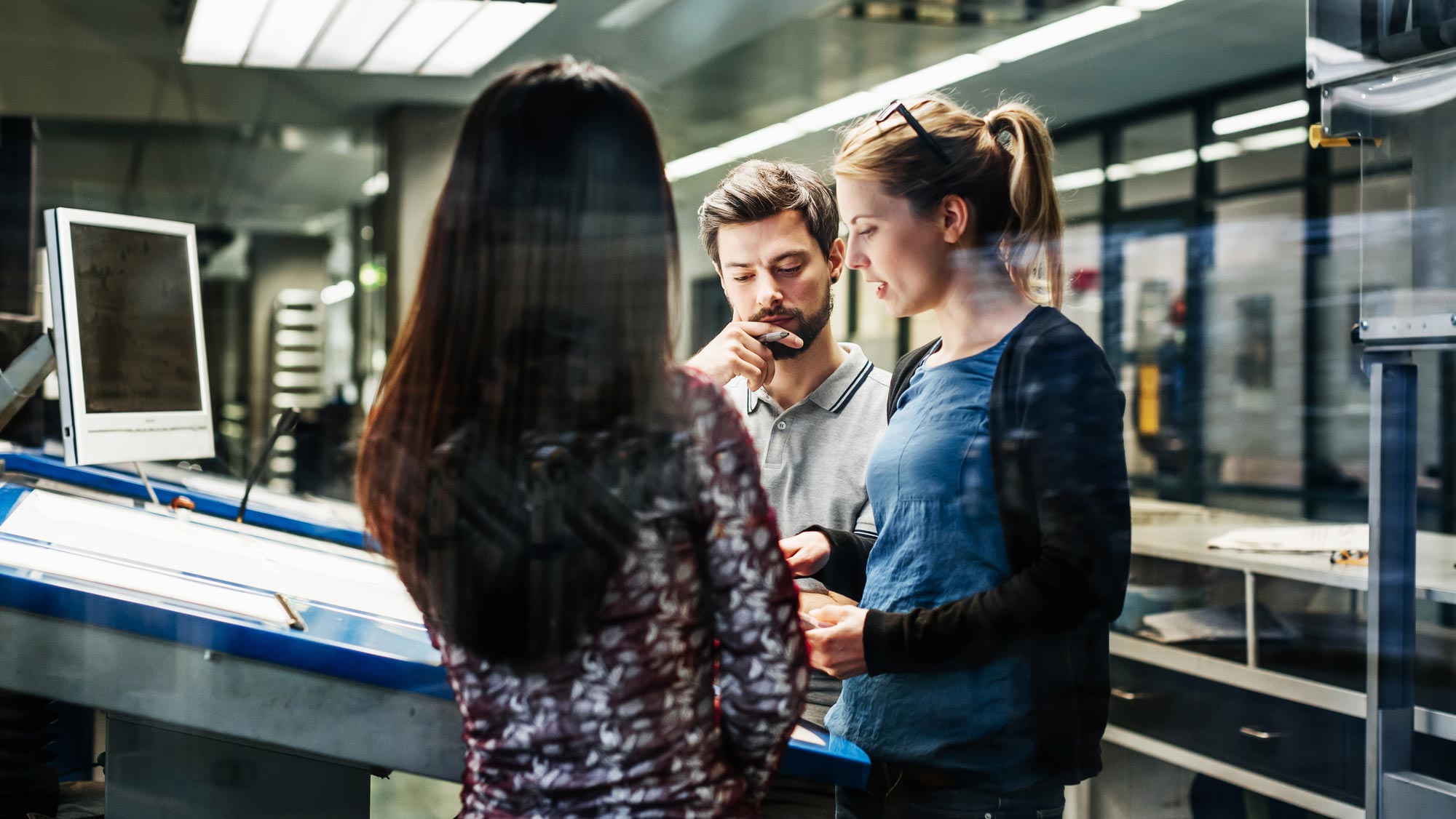 Three people standing in a workspace, having a discussion. 
