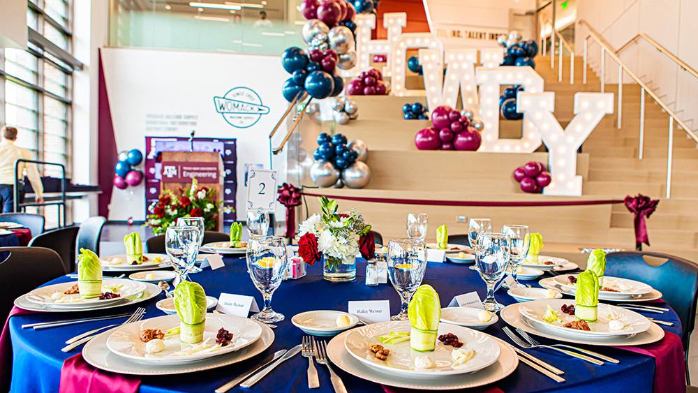 Round set the table with blue table cloth in the foreground with big light-up letters that say Howdy in the background.