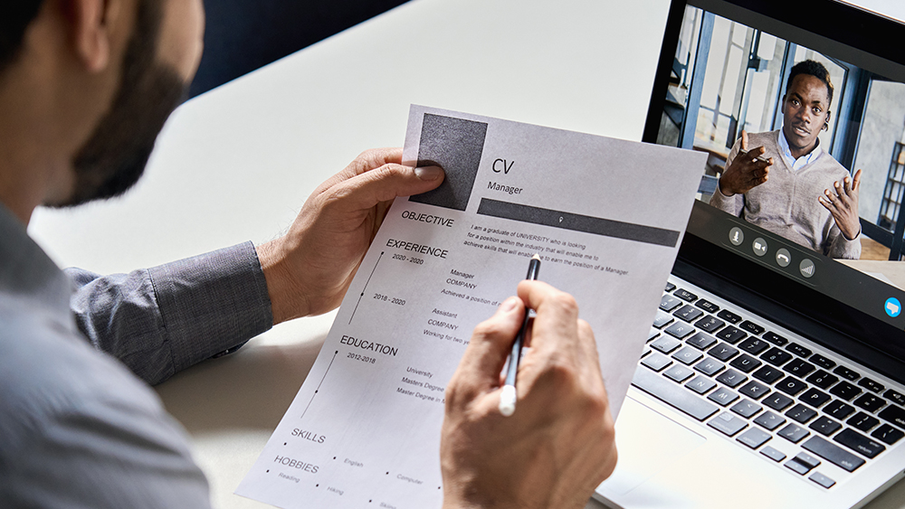 Supervisor conducting a virtual interview with candidate through computer screen holding resume.