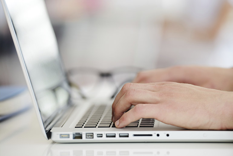 Side view of persons hands on a laptop keyboard