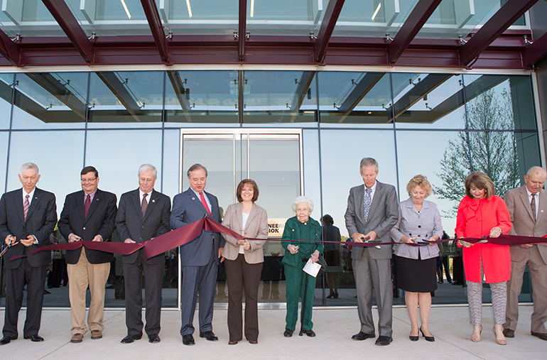 People cutting maroon ribbon at building ceremony