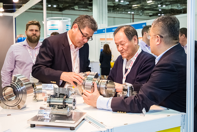 Individuals At A Booth in The Turbomachinery Lab and Pump Symposium Handling A Mechanical Device