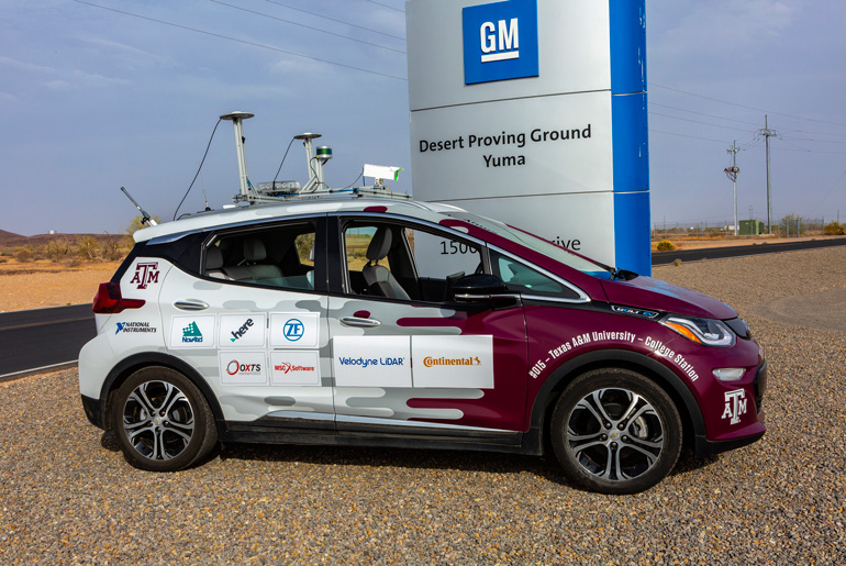 Auto drive car with A&amp;M logos and sponsor logos parked in front of General Motors sign.