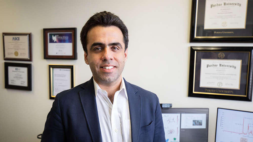 Dr. Ali Mostafavi stands in front of a wall of awards.