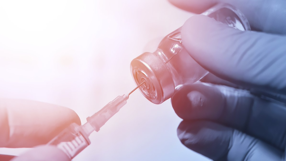 Close-up of hands in latex gloves holding a syringe in one hand and a vaccine bottle in the other.