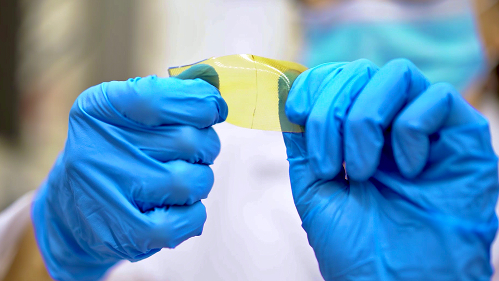 Close-up of two hands wearing blue latex gloves demonstrate flexibility of a new family of polymers that can self-heal, have shape memory and are recyclable.