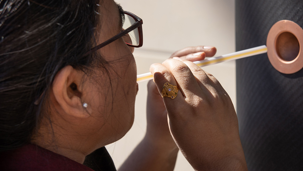 A young woman wearing glasses blowing through a straw into the new COVID-19 breathalyzer.