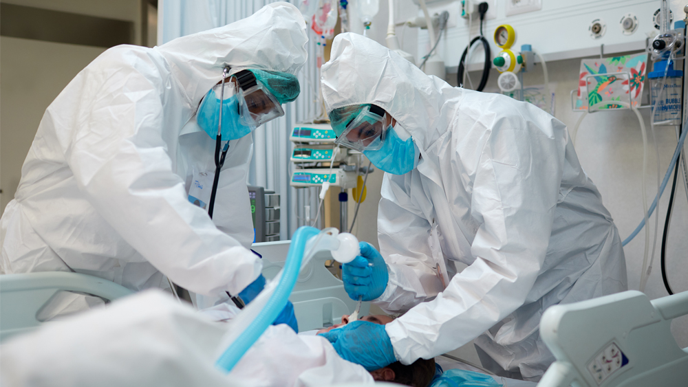 Two hospital staff work to intubate a patient lying in a hospital bed.