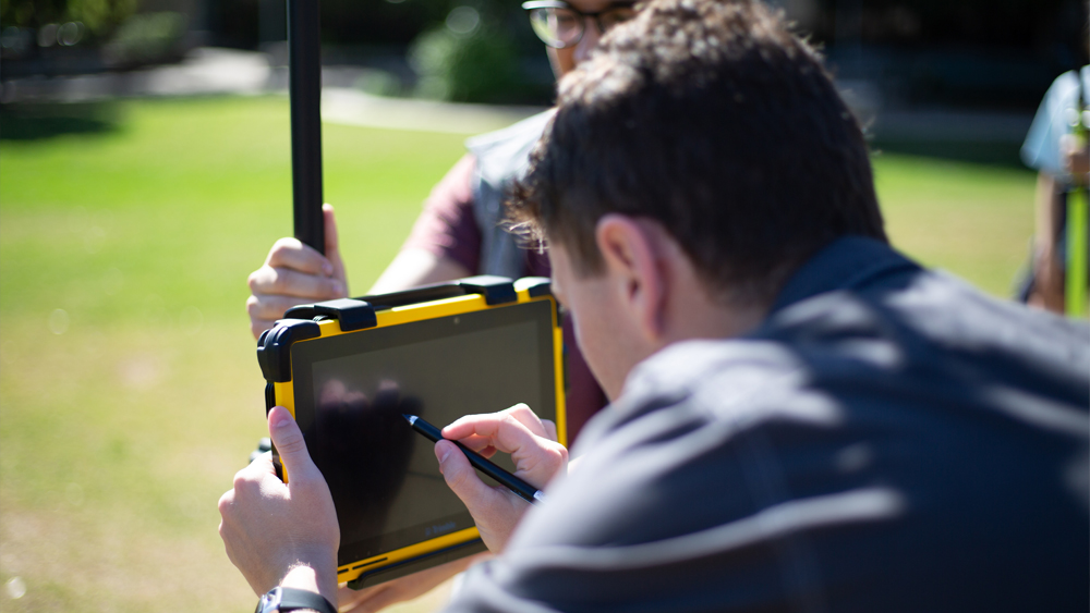 Two men in a grassy field looking at an iPad.