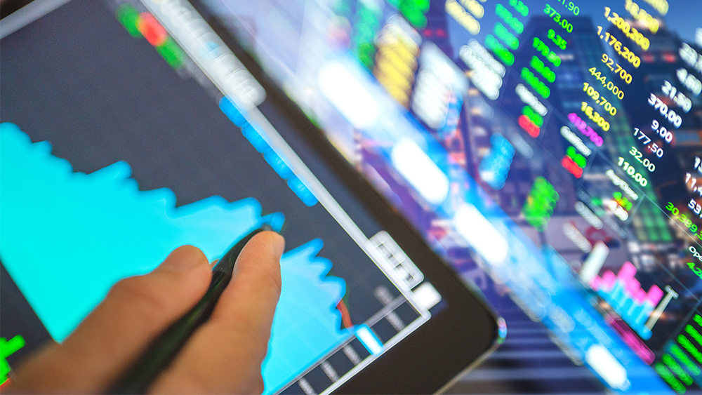 A hand in front of a monitor showing tabulated data.