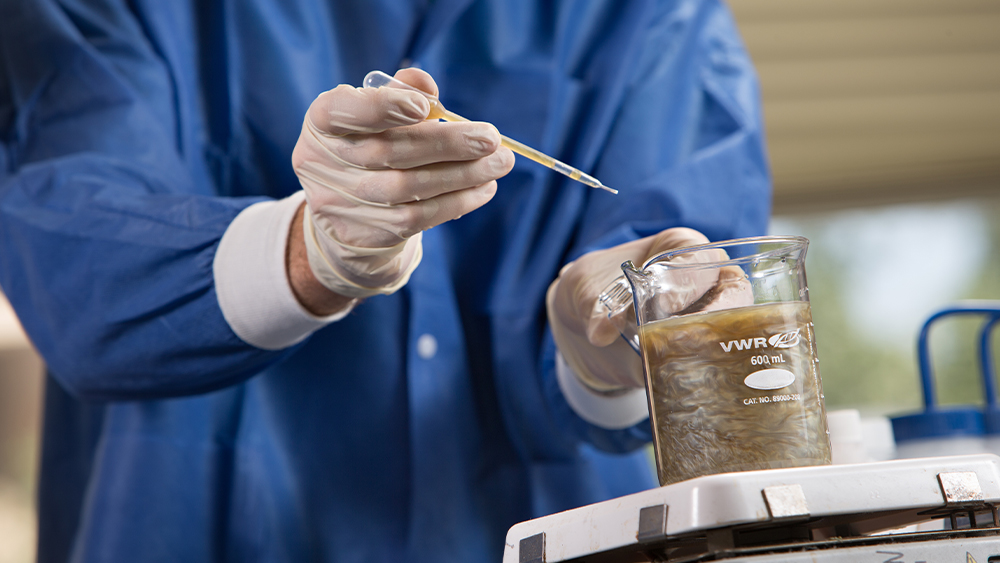 Person in the lab using a pipette to drop a solution into a full beaker 