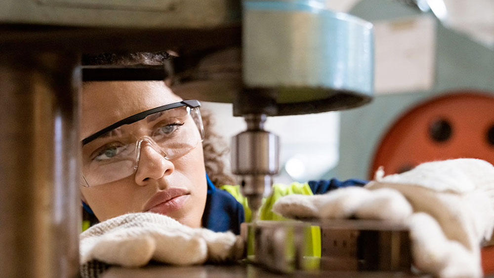 Woman cutting out metal figure with large piece of manufacturing equipment.