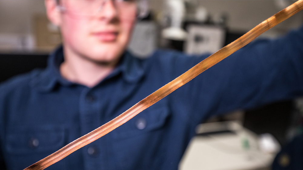 Texas A&amp;M graduate student Matthew Stahr holds a continuous metal strip produced from copper using MetPeel.