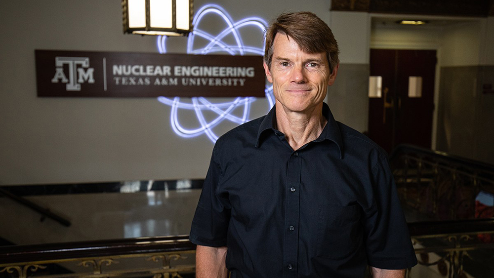Dr. Marvin L. Adams standing in a room with the Department of Nuclear Engineering and a nuclear fission symbol in the background.