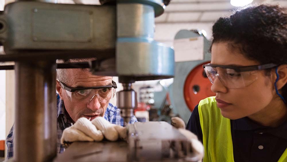 Instructor teaching a female student to use machinery.
