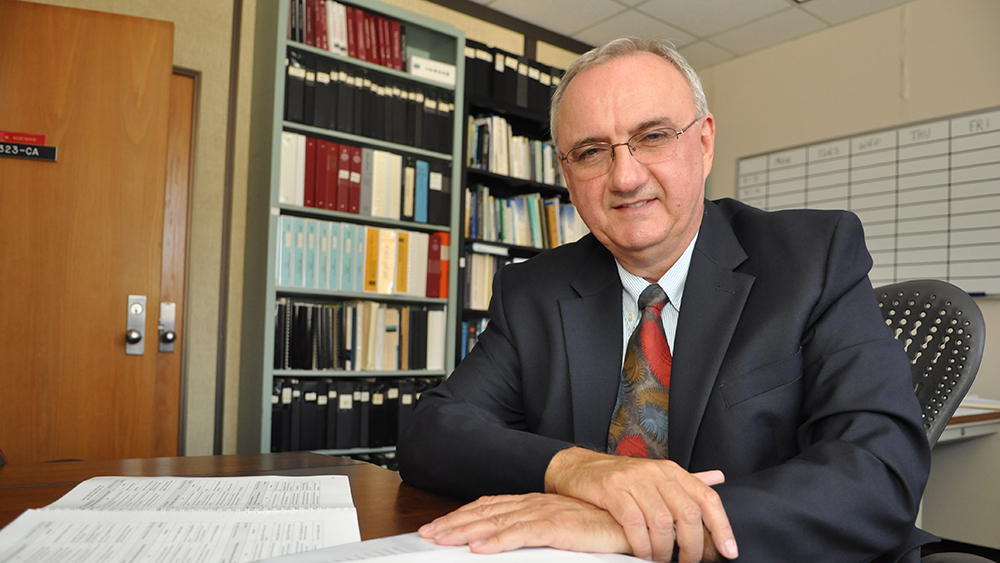 Dr. Mladen Kezunovic sitting at his desk in his office with books behind him.