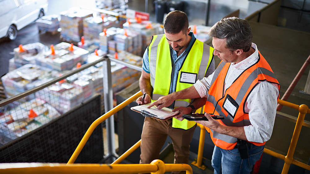 Shot of two warehouse workers standing on stairs using a digital tablet and looking at paperwork
