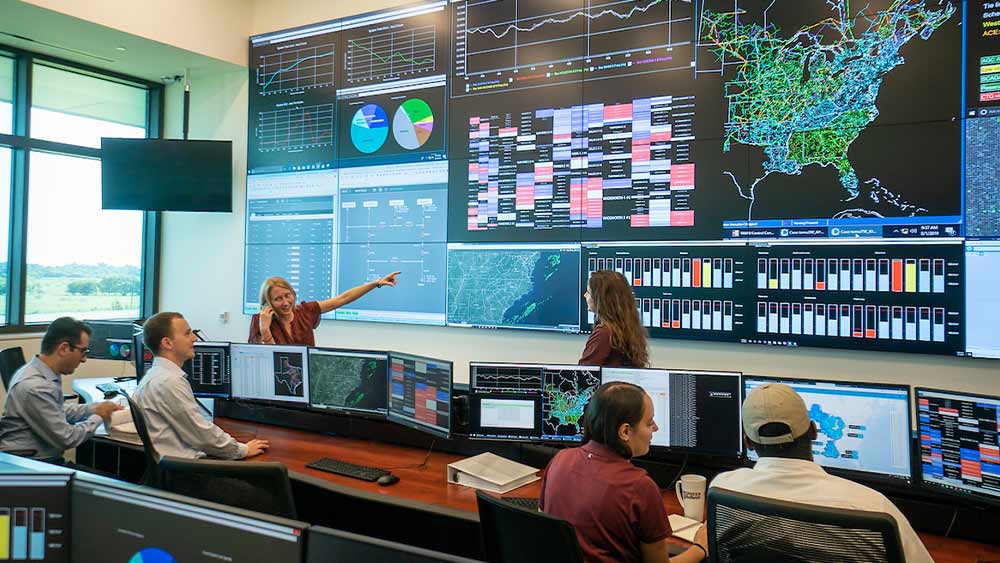 A series of screens displaying energy management systems along the eastern portion of the U.S. with supplemental charts and researchers monitoring activity. 