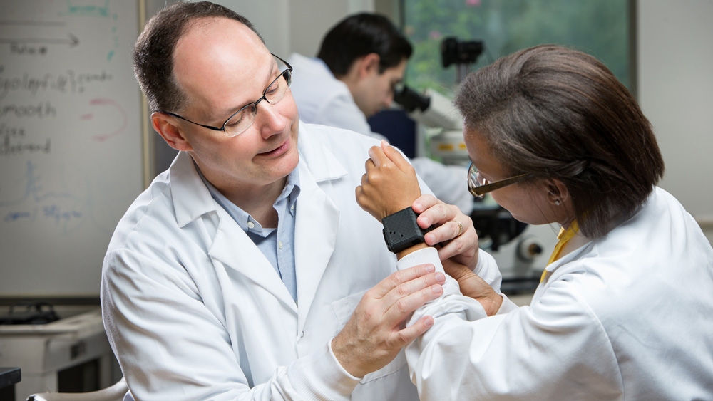 Dr. Cote looking at a wearable device on a student's arm