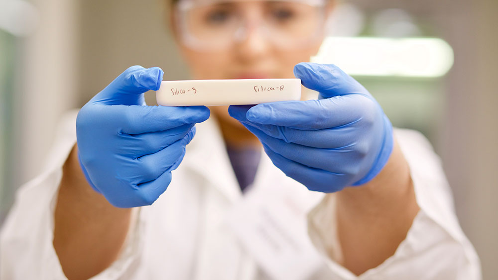 Female in blue lab coat holding up a 3d printed polymer