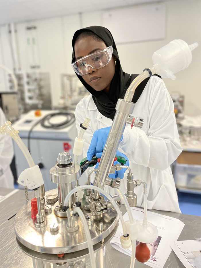Student in a white lab coat using lab equipment.