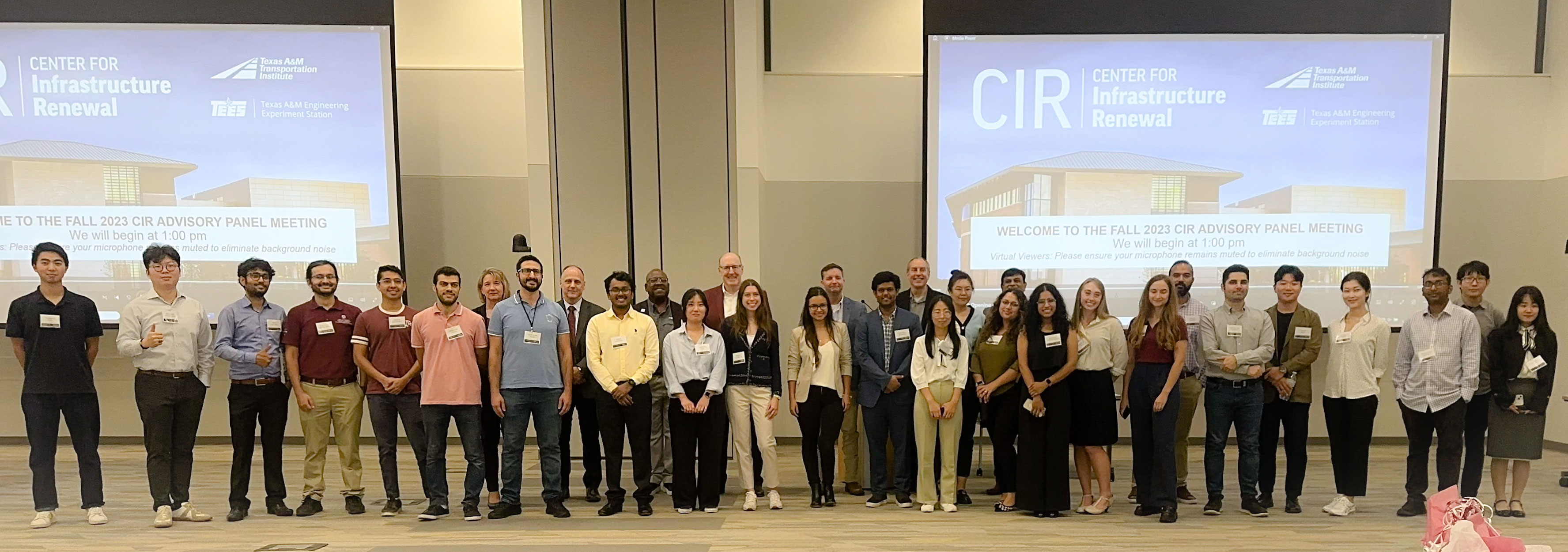 A large group of people standing giving a thumbs up in front of a presentation 