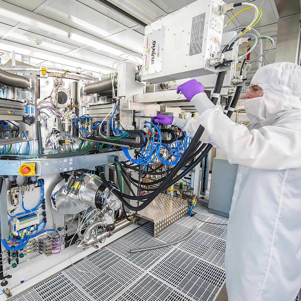 Man wearing protective a lab outfit, gloves, goggles and a face covering working on a machine.